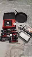 Photo showing portable gas range in red with black case, multiple fuel canisters, Lodge cast iron skillet, RoadPro stove with small pans, solar lantern.