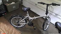 Side view of the silver Stowaway folding bike showing the frame, saddle, rear luggage carrier, and wheels.