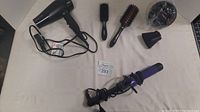 Overview of haircare items including hair dryer, brushes, curling iron, and attachments on beige background.