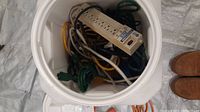 Top down view inside the large white plastic storage bin showing multiple extension cords and beige power strips packed inside