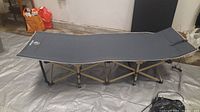 Full side-angle view of the assembled camping cot showing sturdy folded metal support legs and dark gray fabric surface