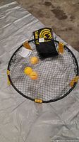 Top down photo of Spikeball round net with black net, yellow straps, three yellow balls, and black carry bag.