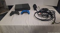 Front view showing console, two controllers, power adapter, and tangled cables on white cloth.