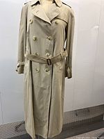 Front view of beige double-breasted trench coat on mannequin showing buttons, collar, belt