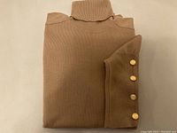 Folded camel cashmere turtleneck sweater showing collar and one sleeve with gold-tone buttons