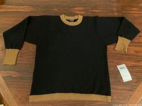 Full front view of black crew neck sweater with camel trim laid flat on wooden surface