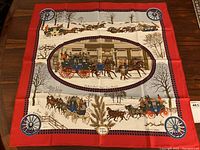Full view of square scarf laid flat showing red border, central winter coach scene and corner wheel motifs