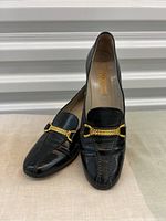 Three-quarter front view of both loafers overlapping, showing overall shape and chain detail