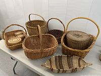 Photo showing 10 assorted vintage and antique wicker baskets in various shapes and sizes arranged on table.