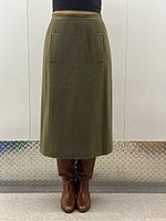 Front view of olive green wool skirt on model showing leather-trimmed waistband and pocket details