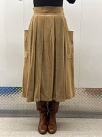 Front view of camel suede pleated skirt on model showing waistband, knife pleats, and front pockets