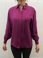 Front view of blouse worn by model showing collared neckline, concealed placket with single visible top button, vertical pleated panels.
