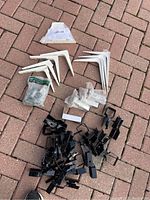 Top view photo showing assorted white metal elbow brackets, black peg brackets, small mounting hardware pieces in bags, and one clear IKEA label.