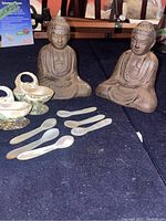 Cast iron Buddha statues with mother of pearl spoons and dishes arranged on a table.