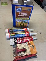 Lot arranged on a table including the Klean Strip Premium Stripper can, three tubes of sealant, and a red caulking tool accessory.