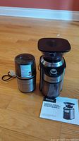 Two grinders on wooden floor including Cuisinart Spice and Nut Grinder and Sboly Coffee Grinder with instruction manual.