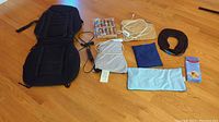 Full view of all items spread on wooden floor including black Homedics back massager, heating pads, inflatable neck pillow, and foot massager.