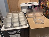 Full layout view showing 12 small square glass cubes in three rows of four, a single medium square glass cube, and two large square glass cubes arranged near each other on a flat surface.