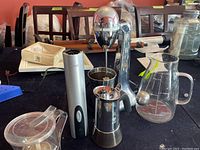 Overview of lot showing Hamilton Beach milkshake maker, tall metallic wine opener, coffee maker, tea sifter, tea infuser ball, and glass pitcher on table
