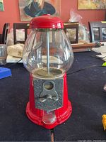 Front view of the vintage red metal and glass gumball machine showing the coin slot, handle and glass globe