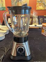 Front view of the Hamilton Beach blender showing stainless steel base, control dial, and glass jar with handle and black lid.