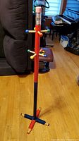 Full view of colorful kid's coat rack shaped like a pencil standing on wood flooring.