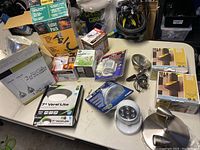 Overview of all light fixtures, light bulbs, and sensors arranged on table including boxed pendant lights, spotlight, cordless light, floodlight fixture, and bulb packages.