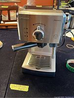 Front view showing stainless steel body with control dial, indicator lights, and attached portafilter.