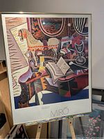 Framed poster showing colorful still life artwork by Joan Miro from 1920, with visible horse figurine, flower, and pipe on table.