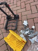 Full set showing the black metal tool dolly, yellow miter box, and a pile of assorted metal rafter ties on a brick patio surface.