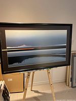 Framed abstract landscape print depicting water, mountains, and sky with horizontal lines and subtle color gradients.