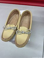 Top view of a pair of light tan women's moccasins showing leather texture and tied leather lace on top.