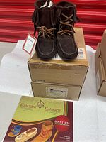 Photo showing one pair of brown suede moccasin ankle boots atop original boxes, along with a catalog or brochure showing moccasin styles