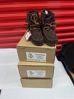 Front view of one pair brown suede moccasin booties on top of three labeled boxes indicating sizes 5, 6, and 7.