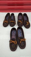 Three pairs of brown suede moccasins with beadwork and rubber soles arranged side by side showing the front and side views.