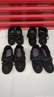 Four pairs of black suede women's moccasins with fringed tops and hand beaded designs.