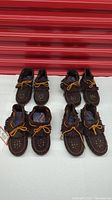 Four pairs of brown suede moccasins arranged in two rows showing front and back views. Each has hand beaded tops and fringe.