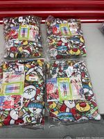 Four packages of Snug as Bug adult Christmas themed fleece footed pajamas showing colorful holiday characters and patterns in original packaging.