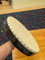 Close-up of side view of one Bodhran showing natural skin drumhead and black frame with metal tuning studs.
