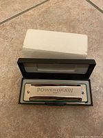 Powerdraw harmonica in an open black plastic case with white lining, showing the metal cover plate with 'Powerdraw' inscription and Brendan Power's signature.