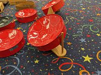 Five red mini steelpan drums on a patterned carpet, three on wooden stands