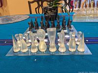 Full view of chess set on blue tablecloth. White (translucent) and black abstract silicone pieces arranged on resin chess board.
