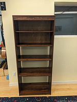 Front view of bookshelf showing five shelves with laminate finish and partial back panel on top three shelves