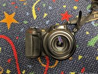 Front view of Fuji FinePix S7000 digital camera showing lens, grip, and Fuji strap attached.