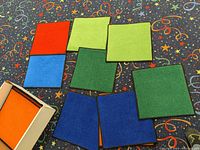 Various colored square floor mats arranged on patterned carpet, showing red, blue, orange, green, light green colors and dark edge binding