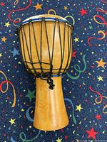 Photo of djembe drum showing wooden body, black ropes, and ripped light-colored drumhead from side angle.