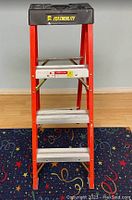 Front view of Featherlite 4-foot fiberglass step ladder showing red fiberglass frame, aluminum steps, and black multifunctional top with tool slots.