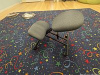 Side angle of kneeling chair showing padded seat and knee cushions on metal frame with wheels.