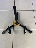 Top view of the black and yellow Hercules mini guitar stand showing its three legs and backrest arm extended.