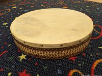 Full side view of the drum showing wooden body with intricate geometric patterns and leather skin head.